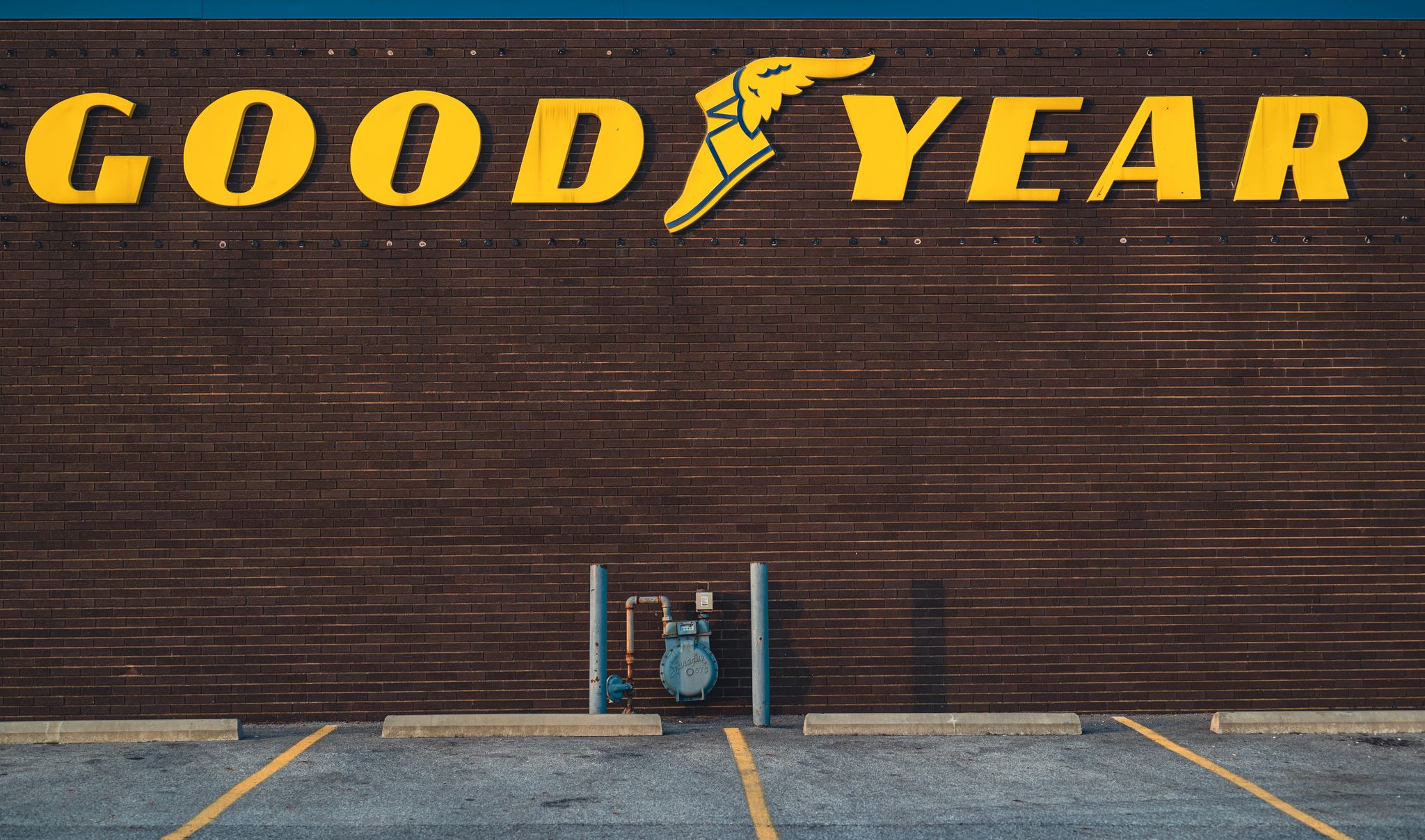 A brick wall featuring a Goodyear sign above an empty parking lot.