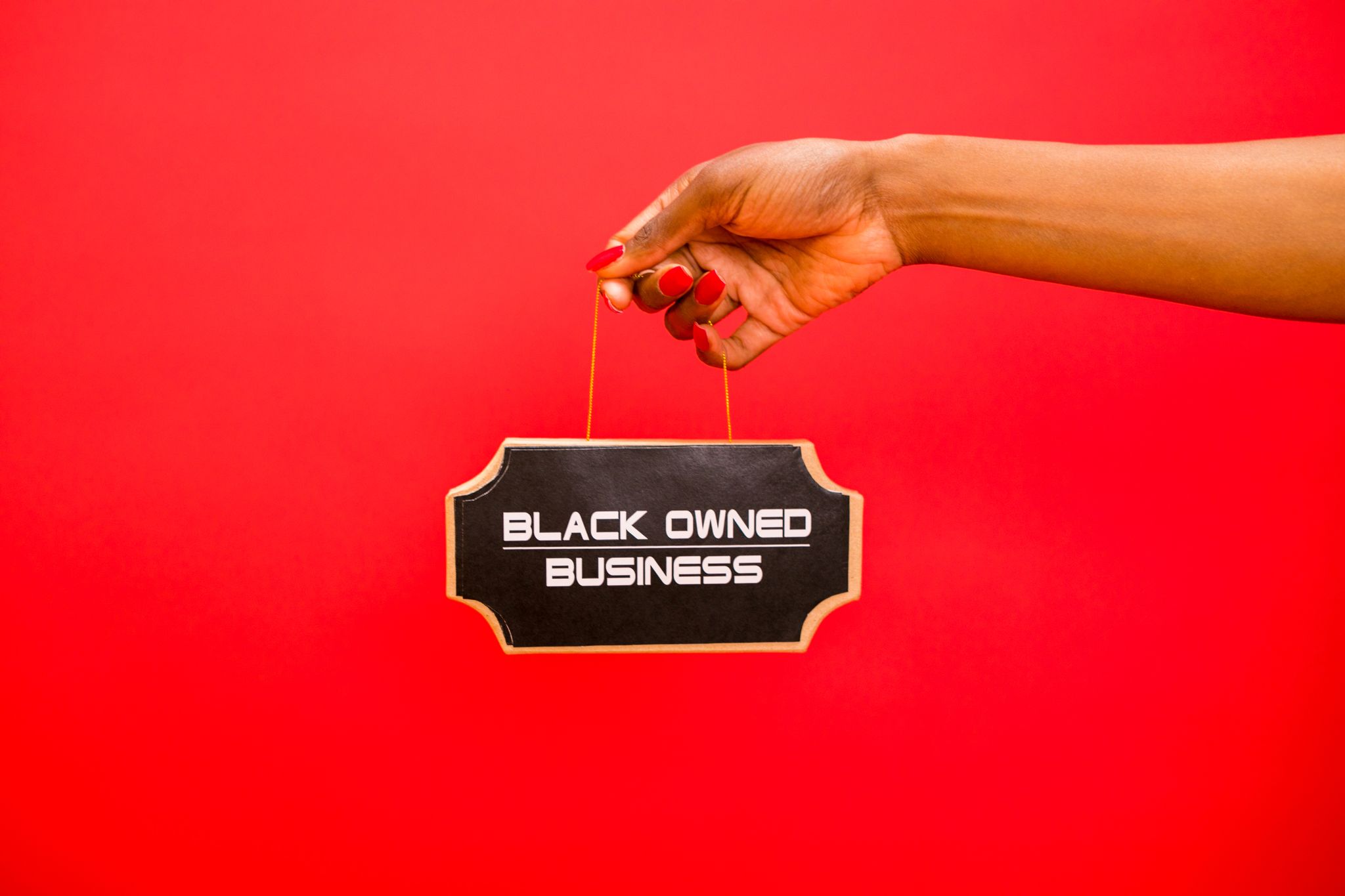 A hand holding a sign with 'Black Owned Business' text against a red background.