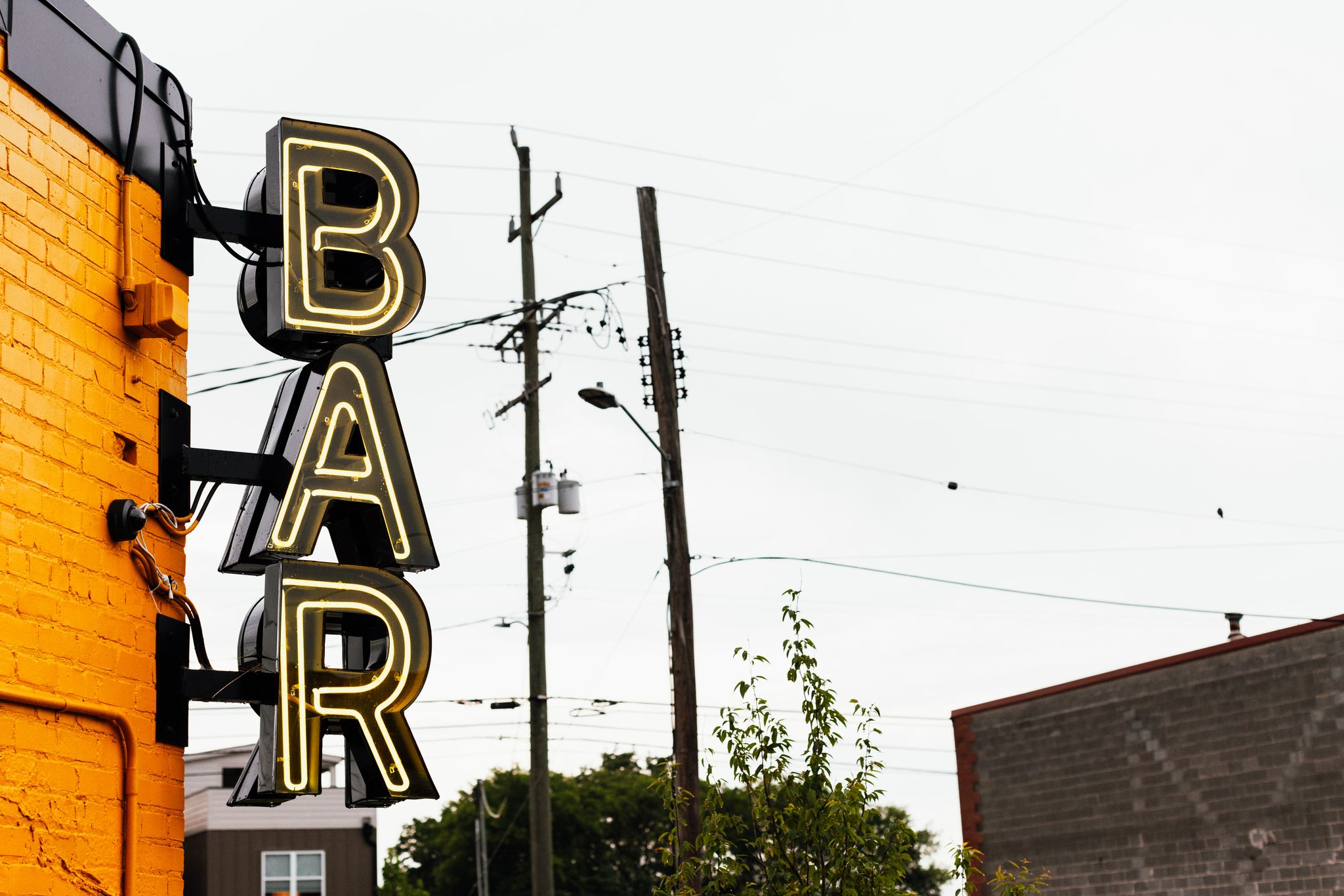A neon bar sign on a yellow brick wall with urban power lines in Chattanooga.