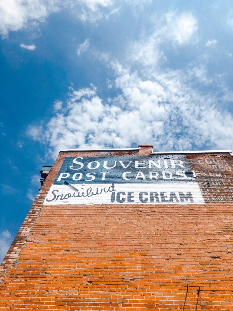Low-angle view of a vintage painted advertisement on a brick wall against a blue sky.
