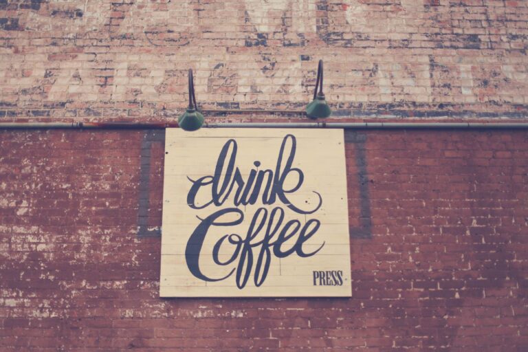 Vintage 'Drink Coffee' signboard on brick wall with green lamps.
